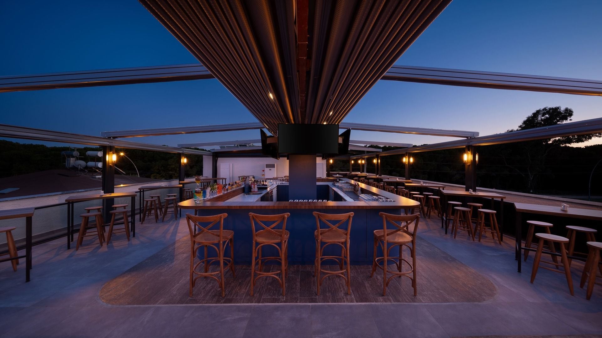 An outdoor bar area with a central bar, multiple seating options, and a view of the sky.