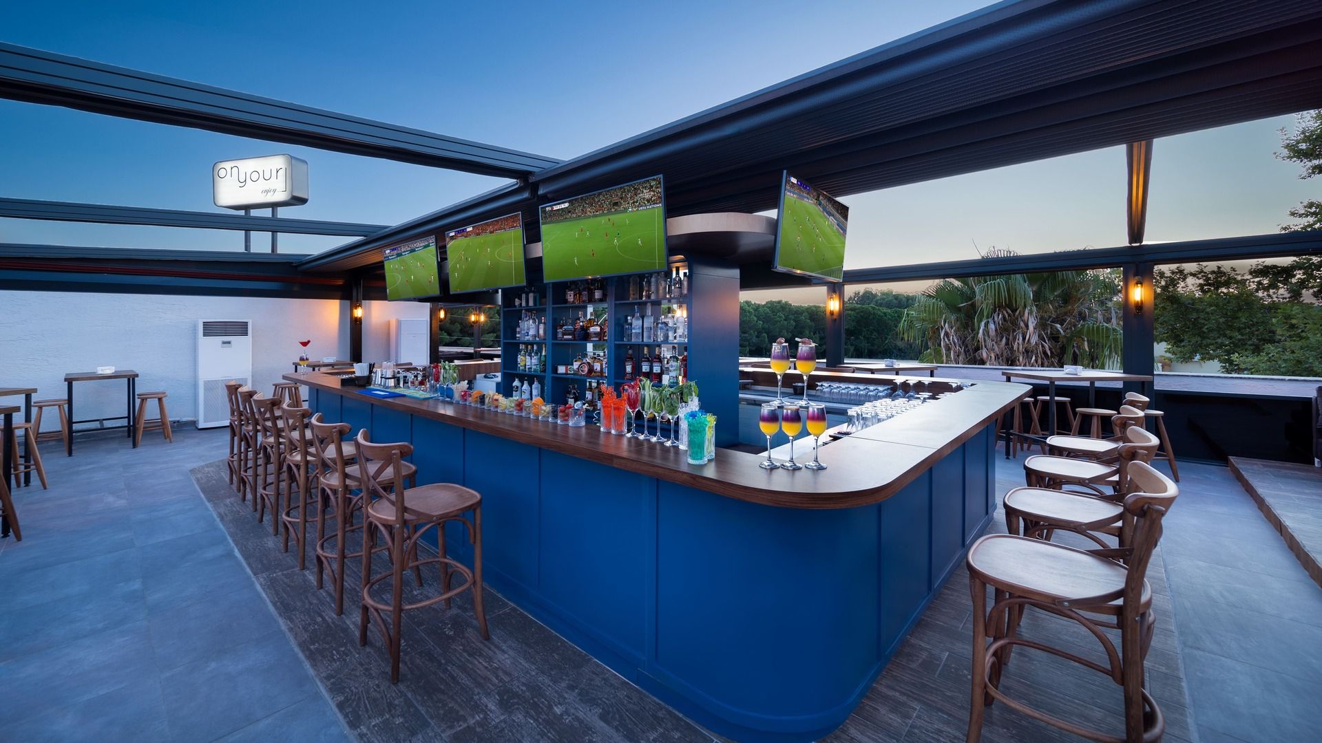 Een bar met een toog, krukken en uitzicht op een voetbalwedstrijd op schermen.