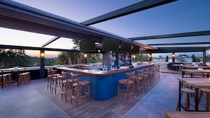 An outdoor bar area with a counter, stools, and a view of the cityscape. - On Your Dreams Belek (Serik)