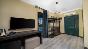 Habitació d'hotel amb televisió de pantalla plana, escriptori amb telèfon i cafetera, armari, porta verda i unitat de climatització.