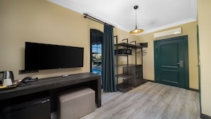 A hotel room with a flat-screen TV, a desk with a phone and a coffee maker, a wardrobe, a green door, and an air conditioning unit. - On Your Dreams Belek (Serik)