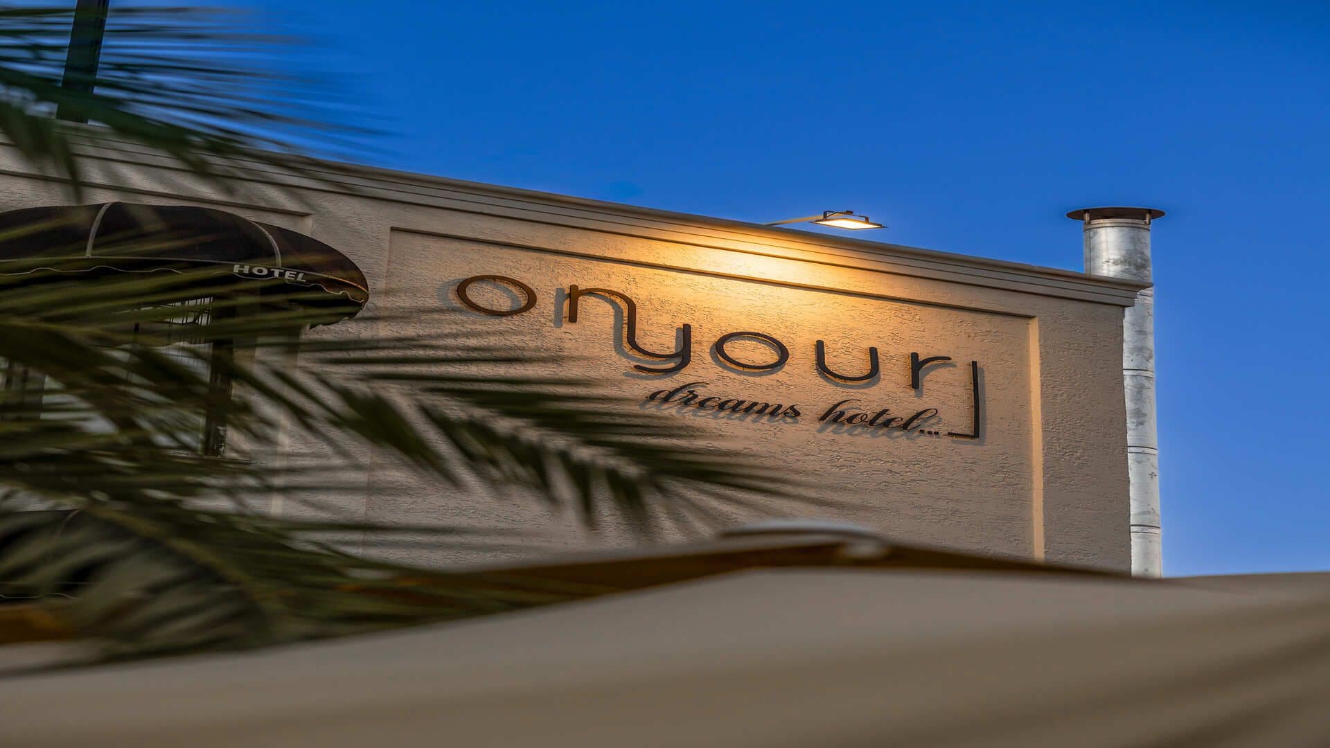 Ein Hotelschild mit dem Namen 'onyour' und dem Slogan 'dreams hotel' vor einer strukturierten Wand.