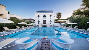 A swimming pool with lounge chairs and umbrellas, a building with a balcony, and a clear sky.