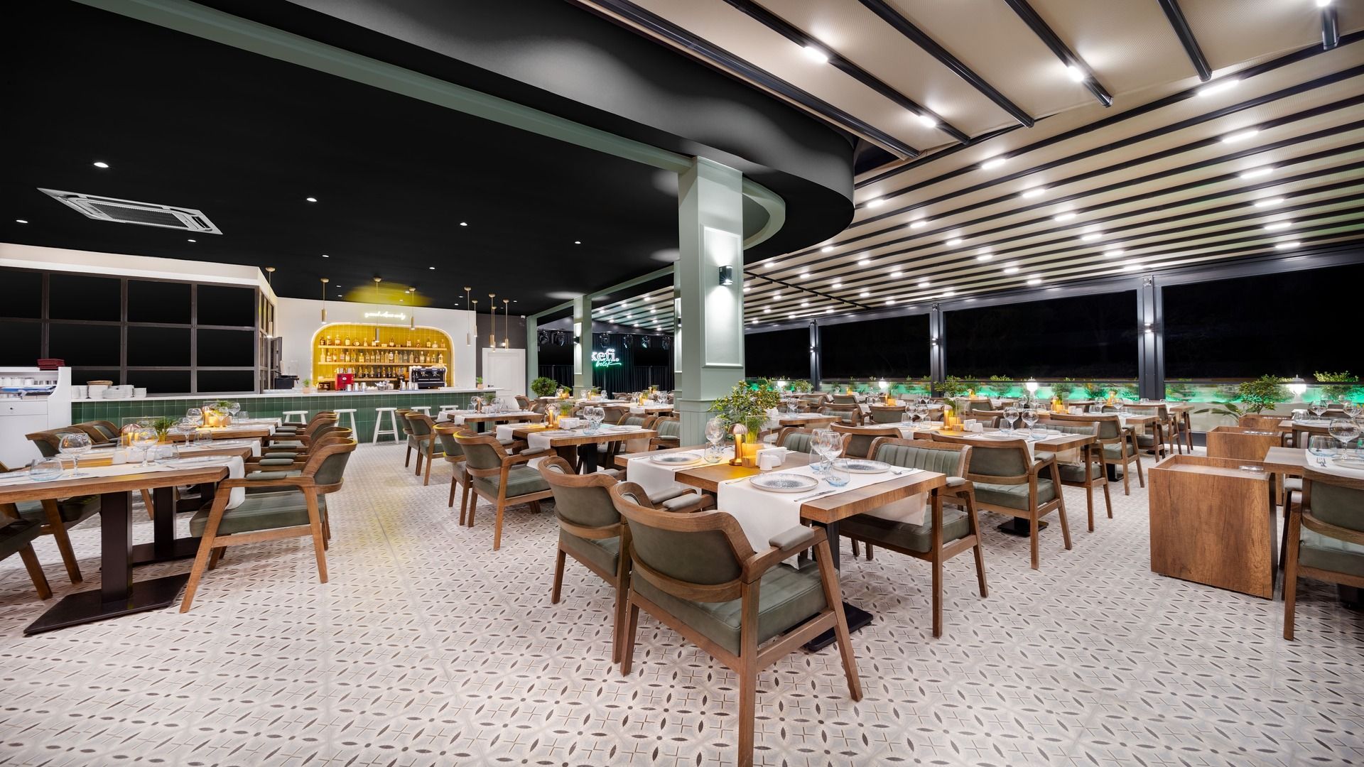 A restaurant with multiple tables and chairs, a bar area, and a view of the night sky.