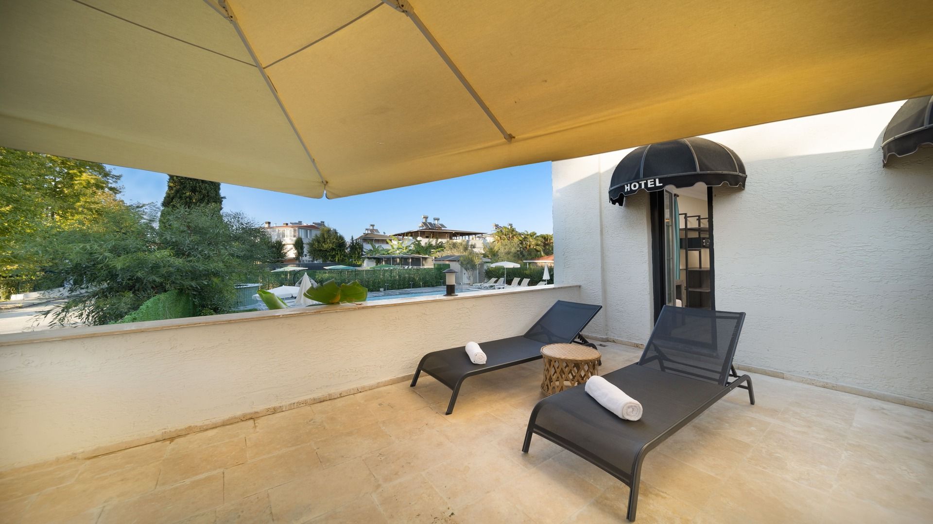 A balcony with two lounge chairs, a small round table, and a view of a hotel and pool area.