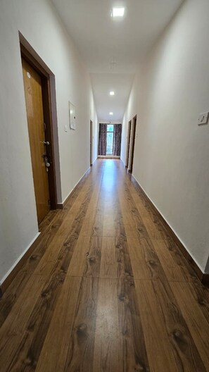 Un couloir au plancher de bois et aux murs blancs, qui mène à une porte au fond.