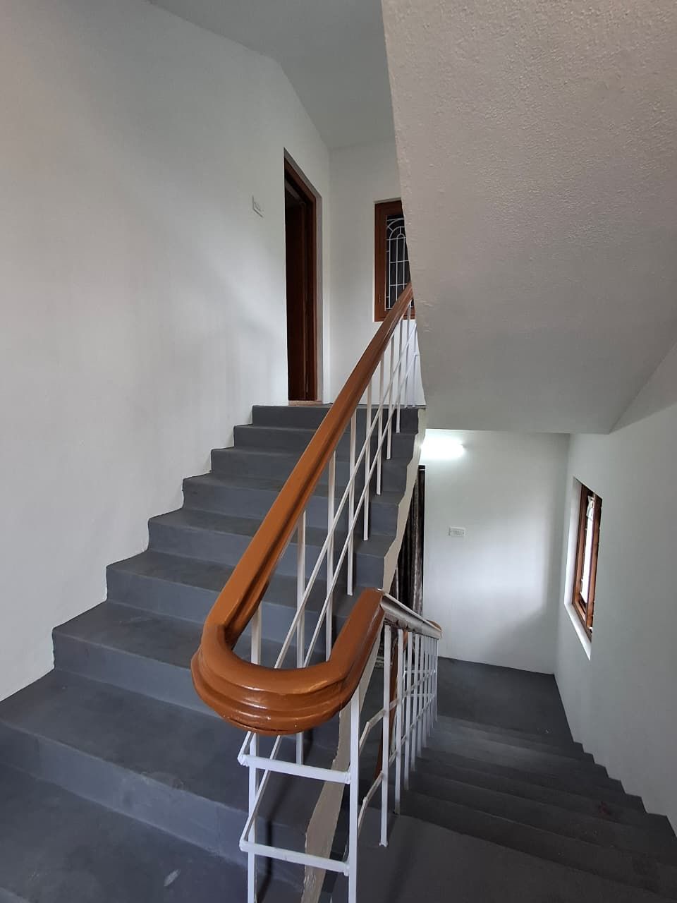 Un escalier avec une main courante en bois et des balustres blanches, menant à un palier doté d’une porte.