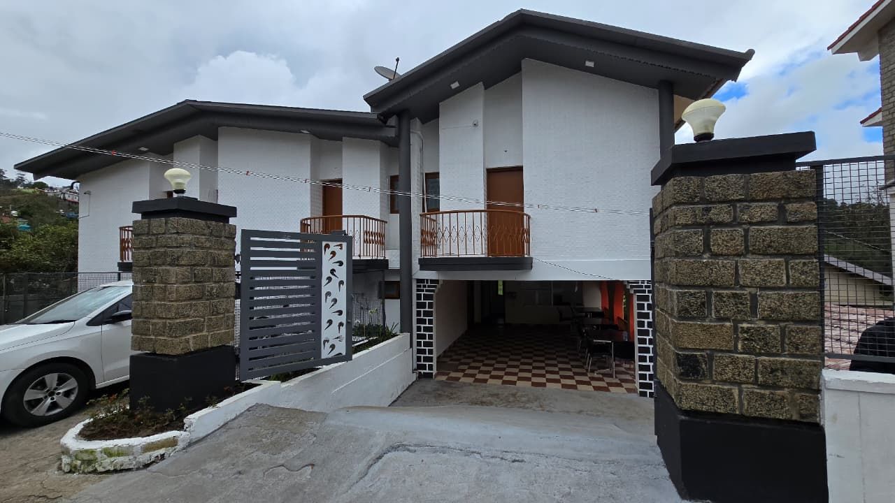 A modern two-story house with a gated entrance, a balcony, and a checkered floor pattern near the entrance.
