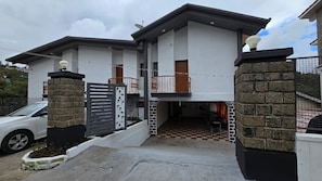 Una casa moderna de dos pisos con entrada protegida por una reja, un balcón y un piso con diseño de cuadros cerca de la entrada.