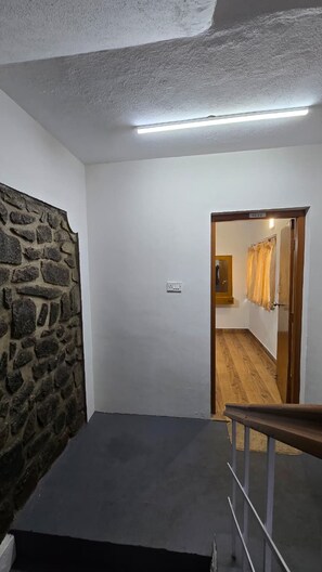 A hallway with a stone wall, a wooden door, and a light fixture.