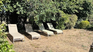 Cuatro sillones de descanso alineados, ubicados en un césped con abundante follaje al fondo.