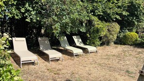 Cuatro sillones de descanso alineados, ubicados en un césped con abundante follaje al fondo.