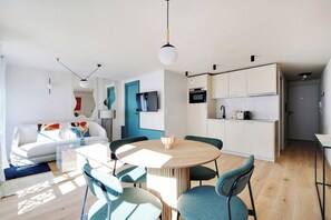 Um espaço de estar moderno com área de jantar, cozinha e televisão na parede.