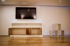 Ein Zimmer mit einem an der Wand befestigten Flachbildfernseher, einem Holzkasten darunter und einem kleinen Tisch mit einer Kiste darauf.