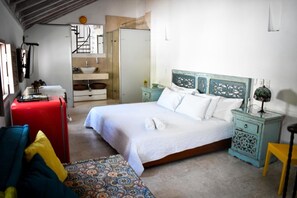 Ein Schlafzimmer mit einem Bett, einem roten Koffer, einer gemusterten Bank und einem kleinen Tisch mit einer Lampe.