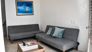 Ein Wohnzimmer mit einem grauen Sofa, einem Holztisch und einem gerahmten Gemälde an der Wand.