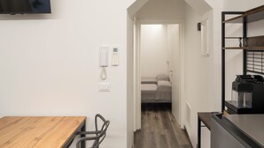 A modern hotel room with a wooden dining table, a built-in coffee machine, and a flat-screen TV mounted on the wall. - Borgo Il Castello, Elsa Apartment (Montichiari)