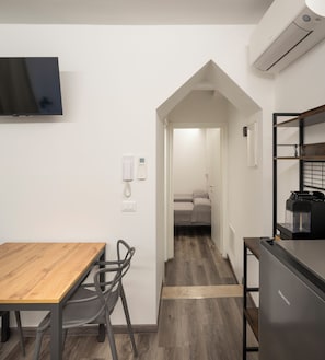 Una moderna camera d'albergo con un tavolo da pranzo in legno, una macchina da caffè integrata e un televisore a schermo piatto montato a parete.