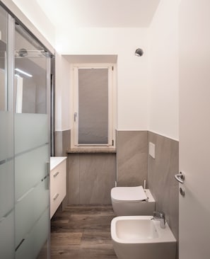 Ein kleines Badezimmer mit Toilette, Bidet und einer Duschkabine aus Glas.