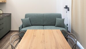 A room with a wooden table, a green sofa, and a kitchenette area. - Borgo Il Castello, Elsa Apartment (Montichiari)
