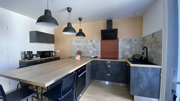 Een moderne keuken met een centraal eiland, hangende lampen en een betegelde achterwand.