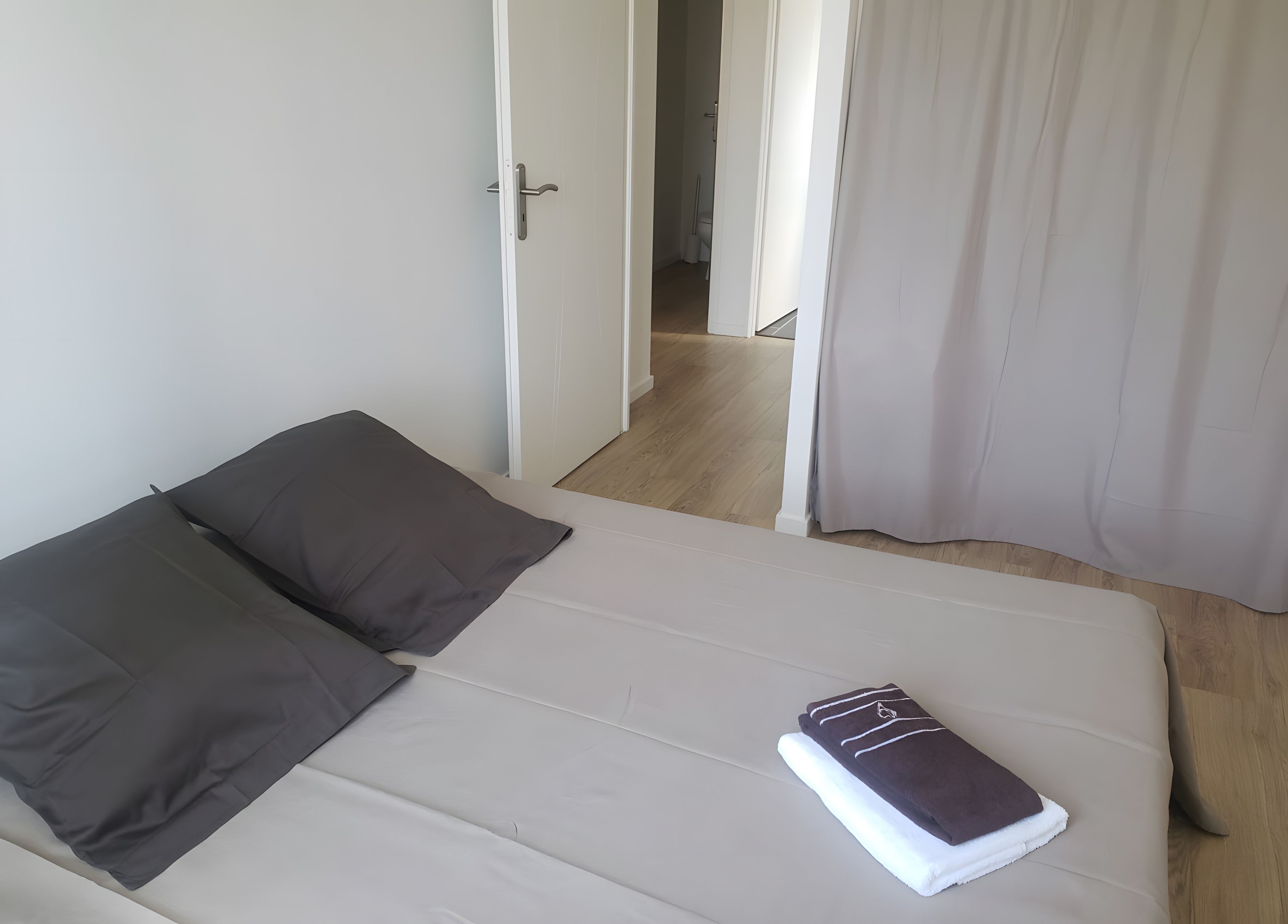 Een bed met een witte matras, twee donkere kussens en een opgevouwen handdoek.