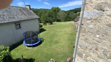 Een gebouw van steen met een gazon, een trampoline en een metalen hek.