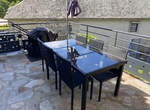 An outdoor patio with a glass table and wicker chairs, a barbecue grill, and a covered umbrella.