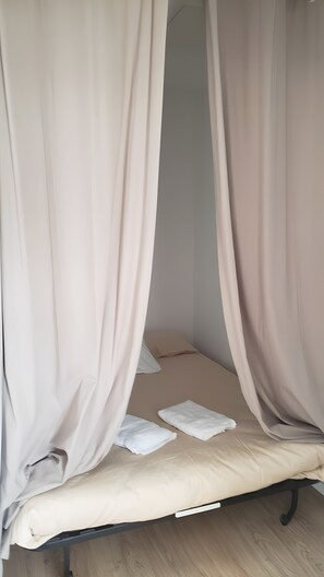 Een enkel bed met een wit matras, beige beddengoed en dunne gordijnen.