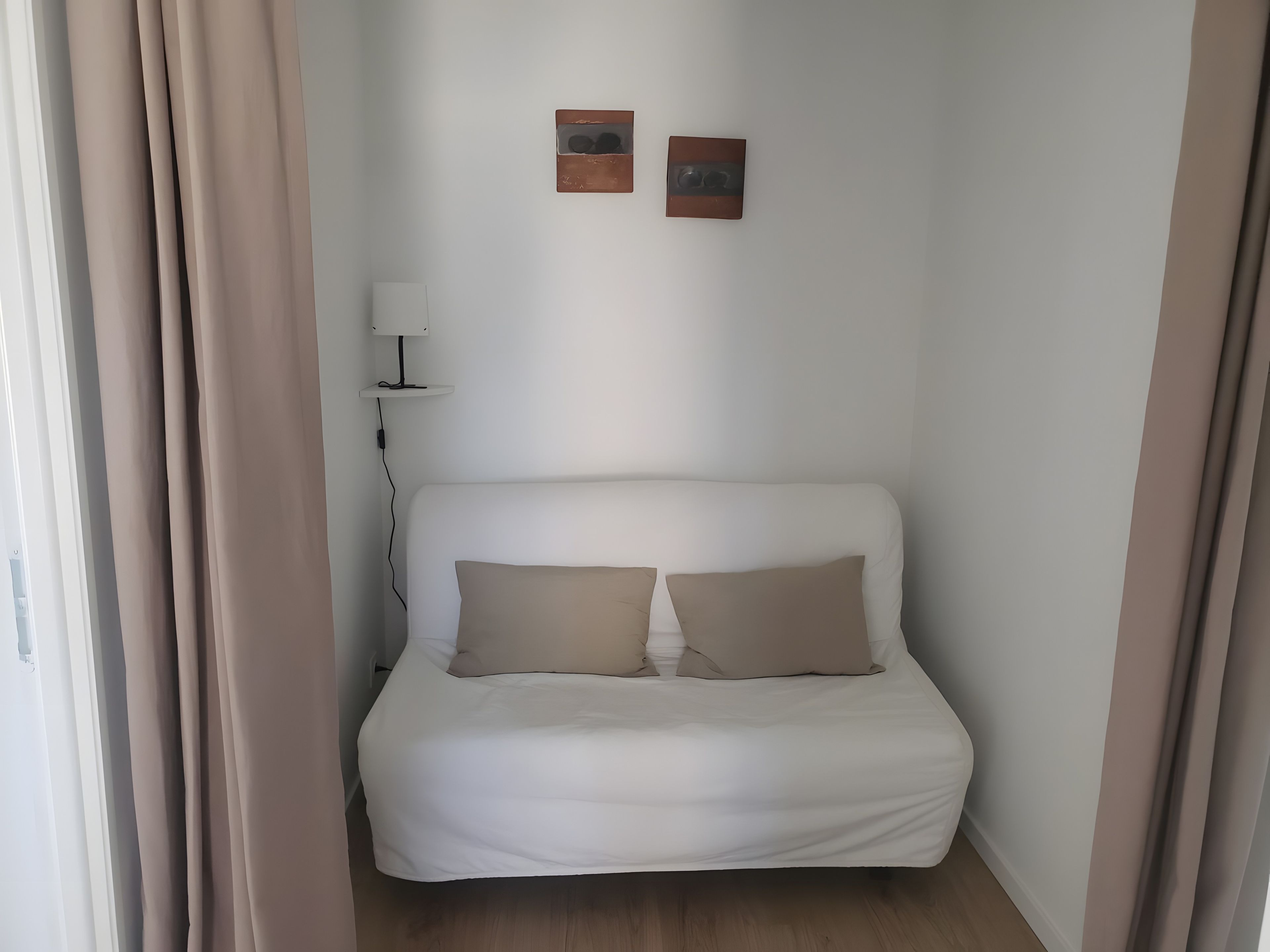 Een eenpersoonsbed met twee kussens, een bedlampje en twee foto's aan de muur.
