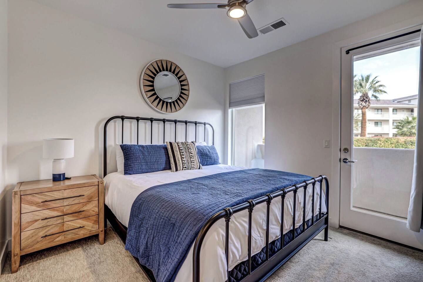 A bedroom with a bed, a bedside table, a ceiling fan, a window, and a door.