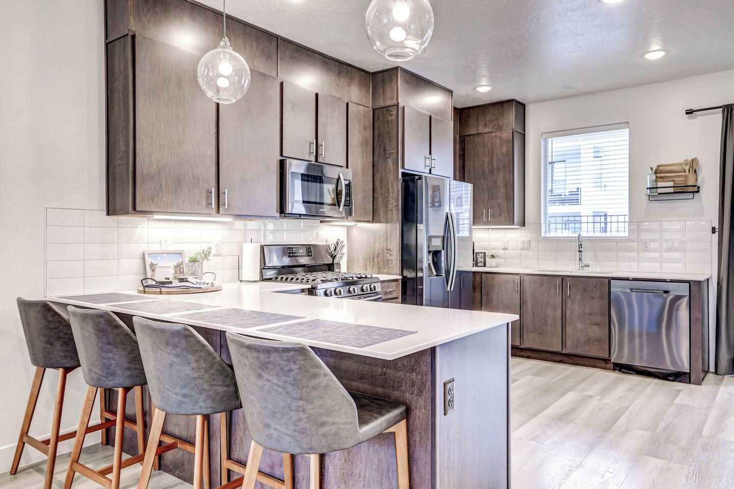 A modern kitchen with a central island, bar stools, stainless steel appliances, and pendant lighting.