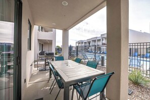 Um pátio com mesa, cadeiras, churrasqueira e vista para uma piscina e edifícios ao fundo.