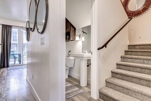 Un interior moderno con un pasillo que conduce a un baño, una escalera y vistas al exterior.