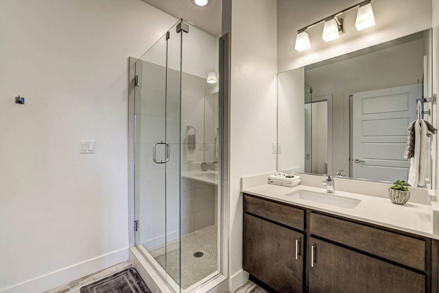 Een moderne badkamer met een douchecabine van glas, een grote spiegel en een wastafelmeubel met donkere houten kastjes.