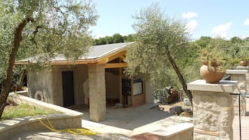 A small stone building with a wooden roof, surrounded by olive trees.