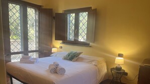A hotel room with a bed, two bedside lamps, a window with shutters, and a wall-mounted clock. - Cà Fondi  (Lazio)