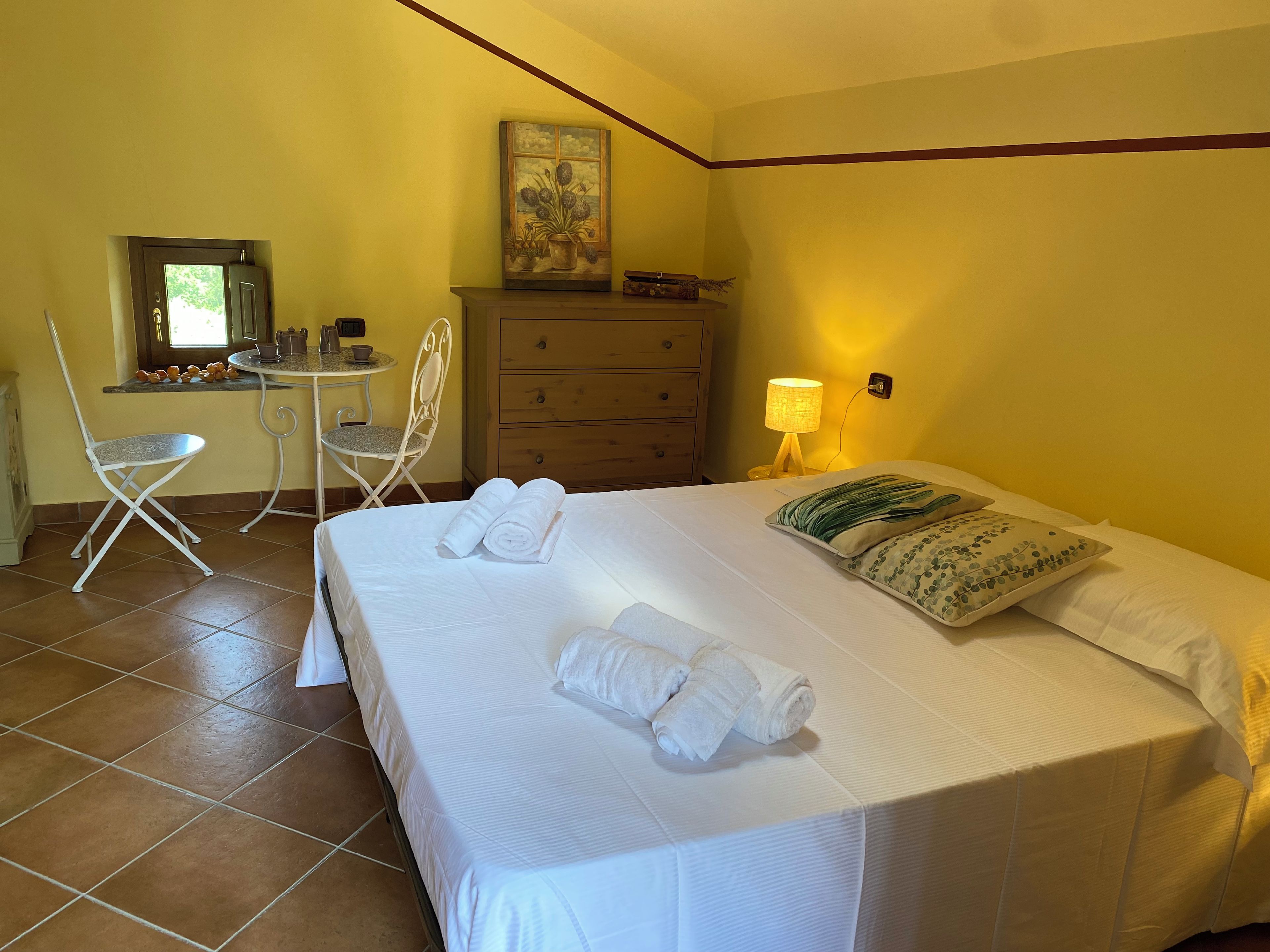 A hotel room with a bed, a desk, a chair, a dresser, and a lamp.