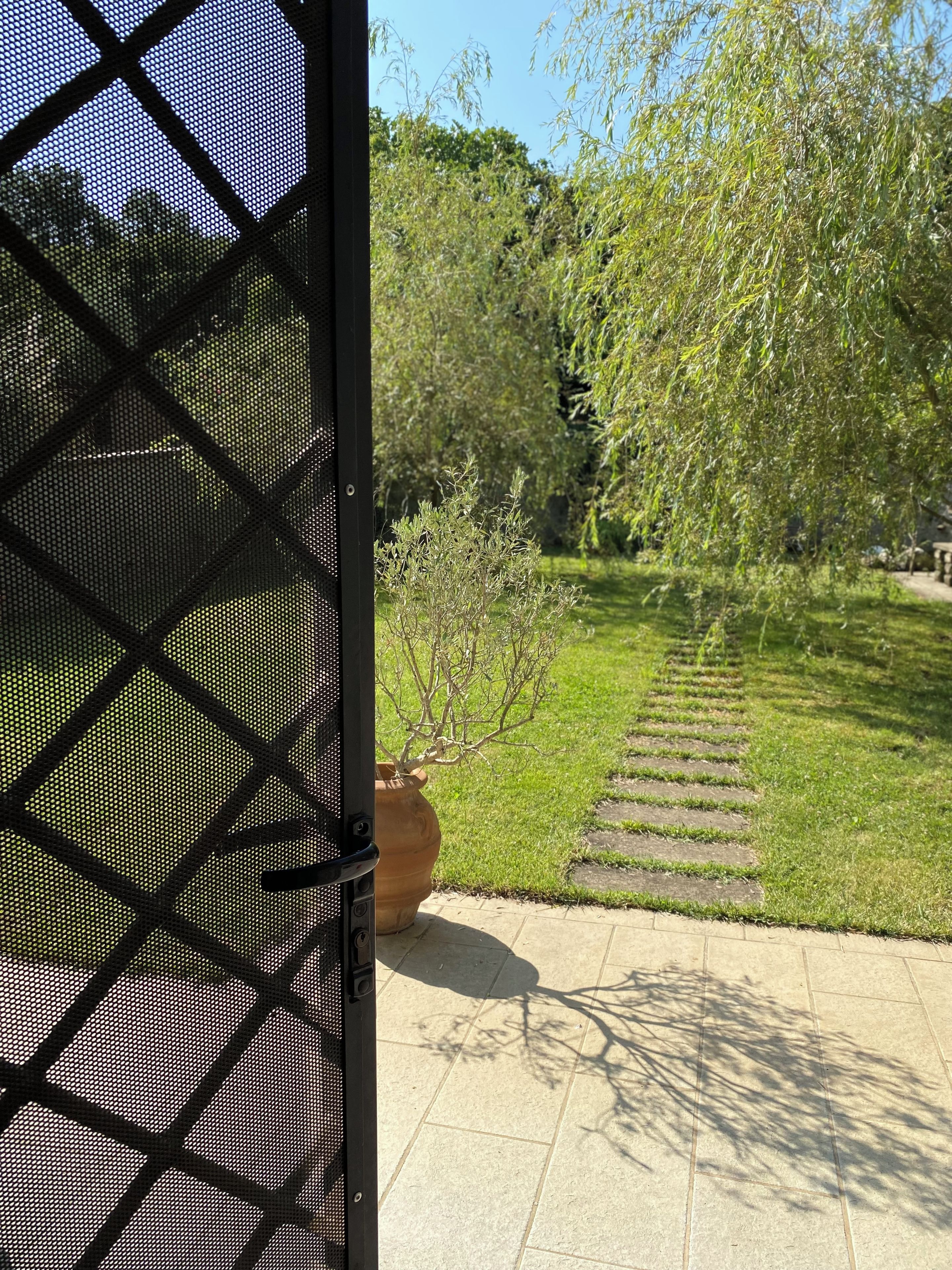 A garden with a paved walkway, a potted plant, and a fence.