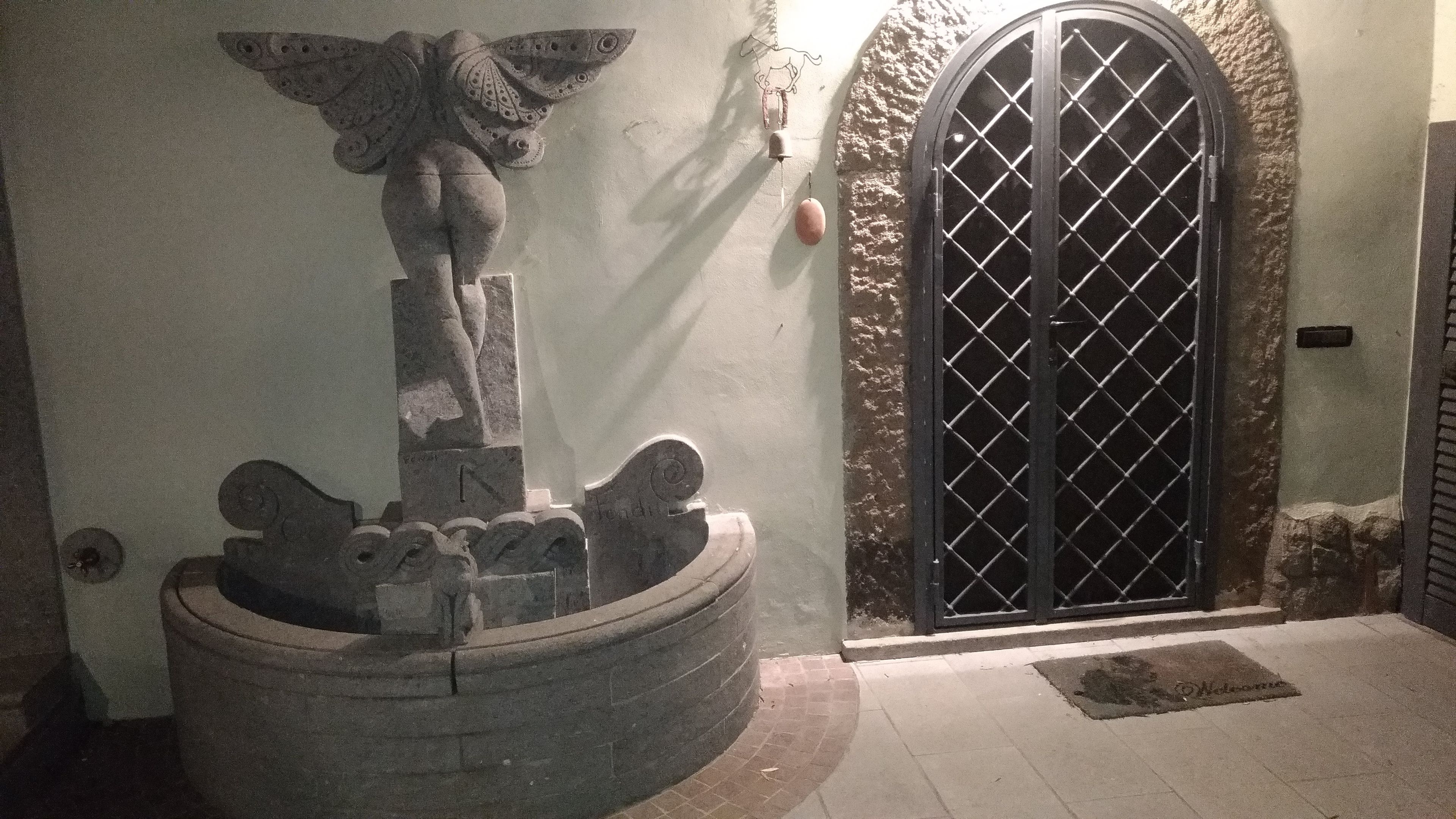 A stone fountain with a statue, a metal gate, and a wall with a textured surface.