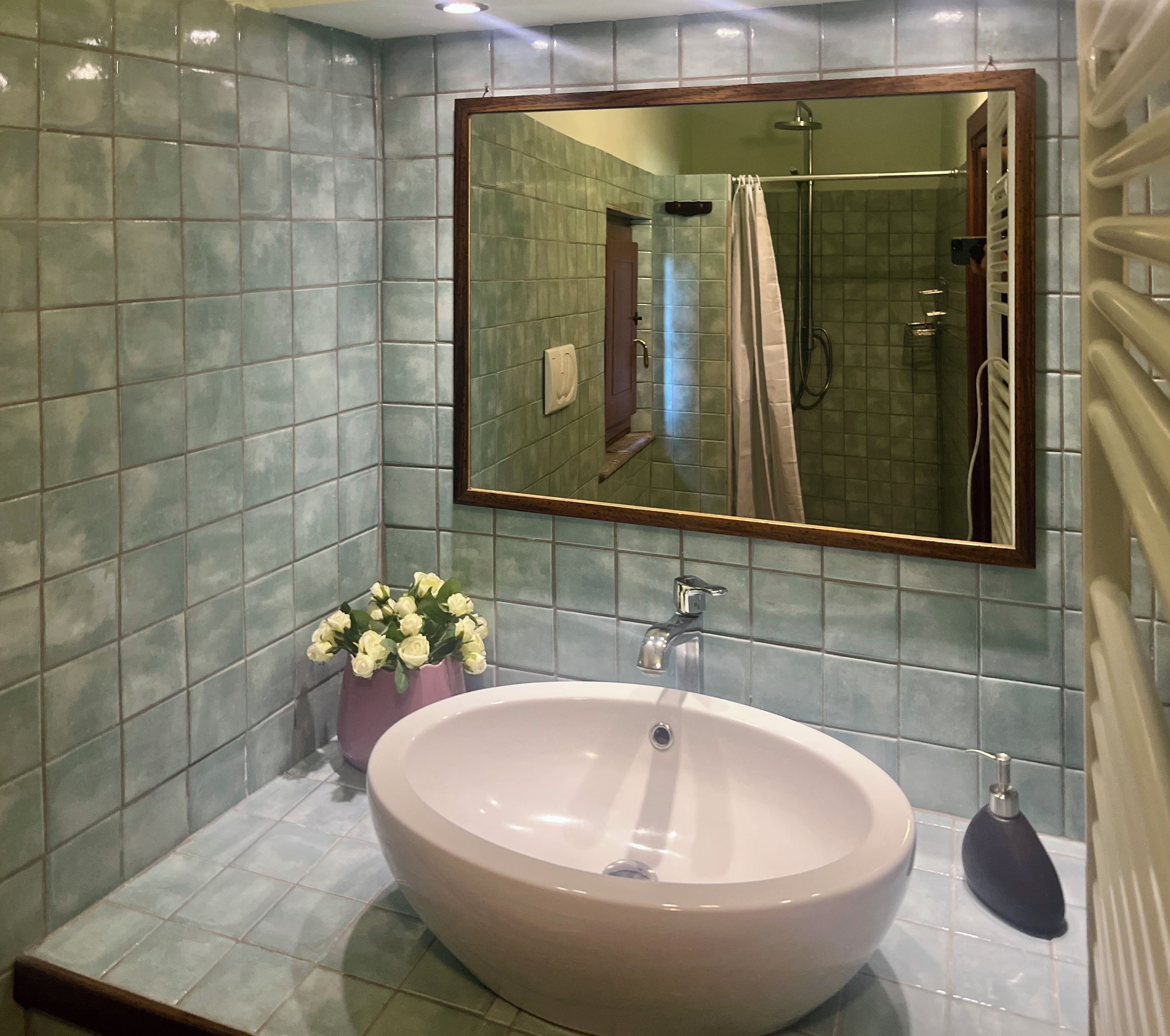 Un baño con un espejo grande, un lavamanos y una zona de ducha.