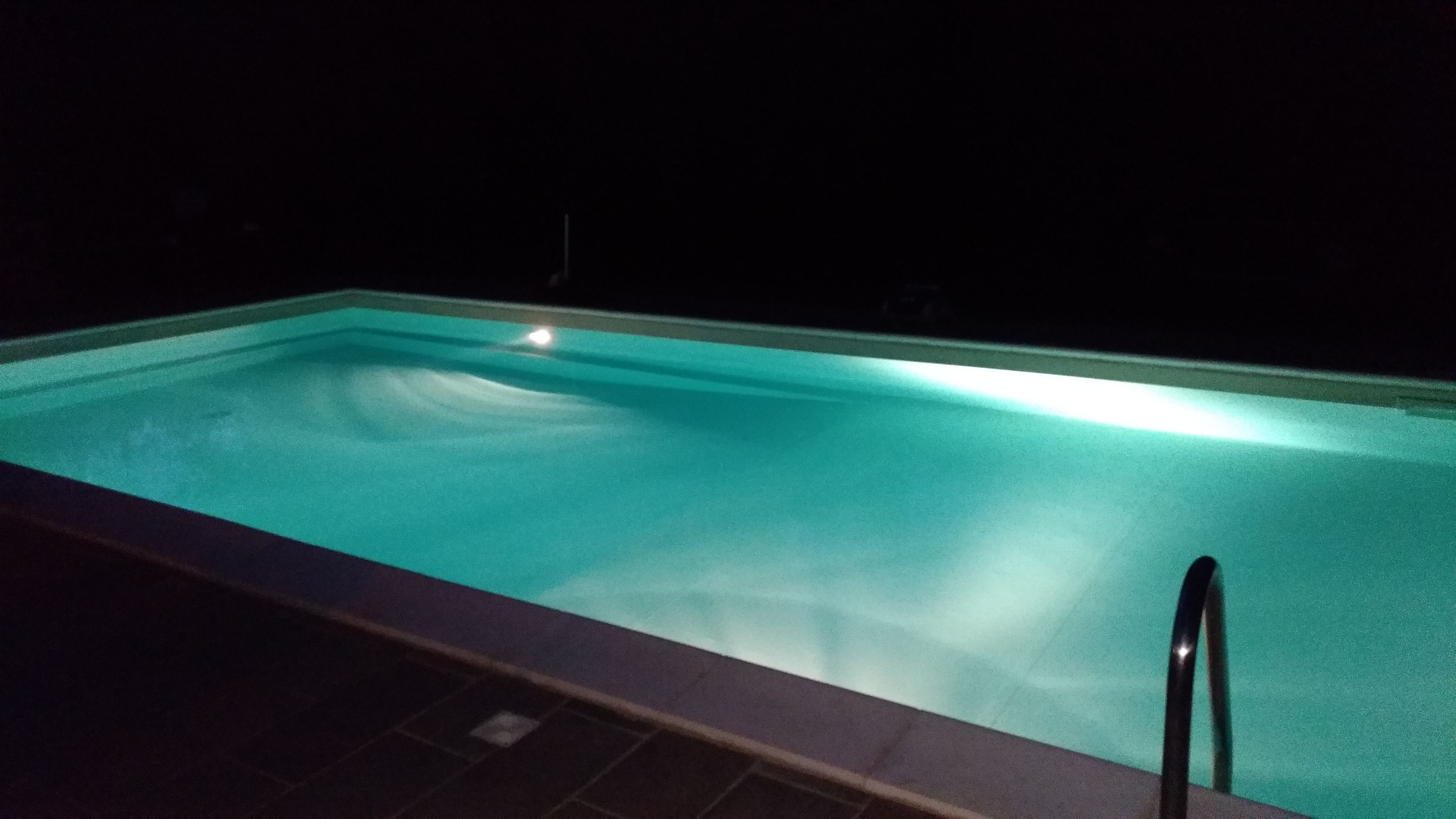Una piscina de noche con borde visible y una única fuente de luz reflejada en el agua.