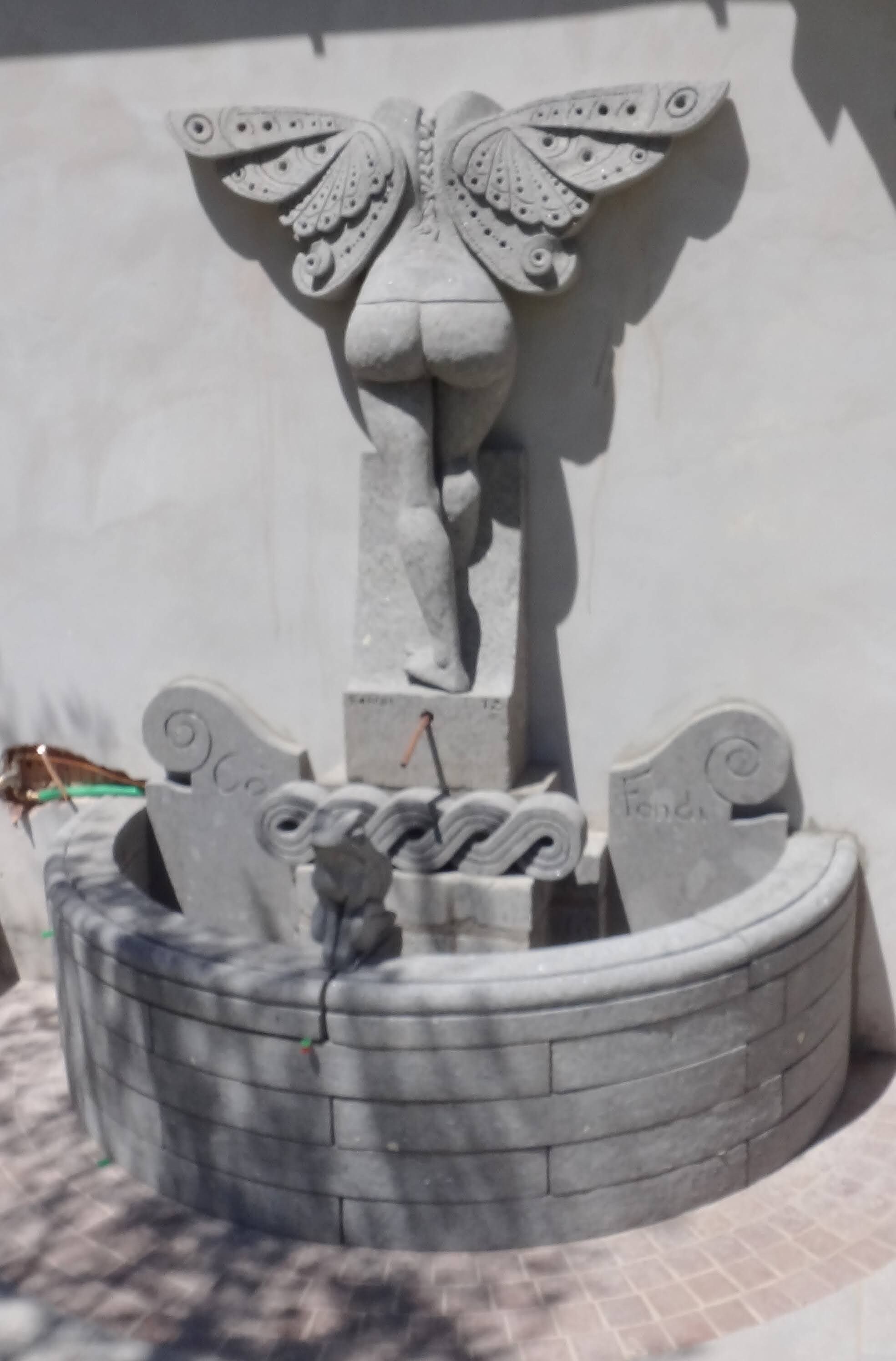Una fuente de piedra con una escultura de mariposa, un cuenco circular y dos placas con inscripciones.