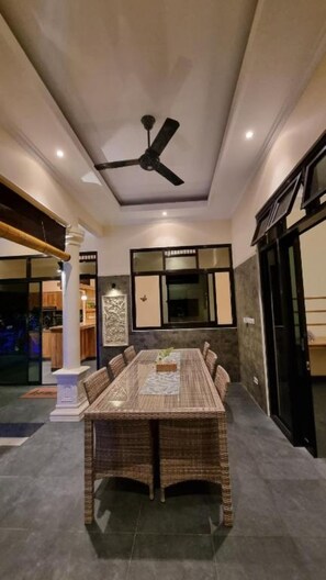 A dining area with a large table, ceiling fan, and a view of the kitchen. - Charming Private Pool Villa in Lovina - Quiet Bali Escape (Buleleng)
