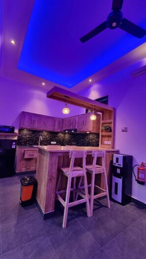 A kitchen with a bar area, wooden cabinets, a ceiling fan, and a fire extinguisher. - Villa Kupu-Kupu 2B – Charming Private Pool Villa in Lovina (Buleleng)