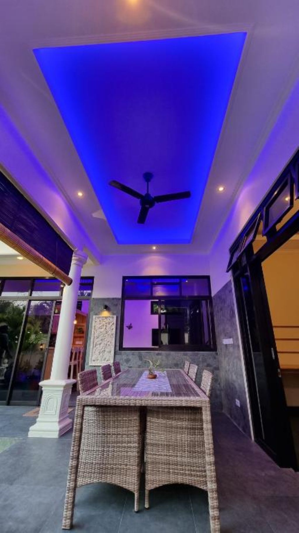 An outdoor dining area with a ceiling fan, a table with chairs, and a view of the outside.