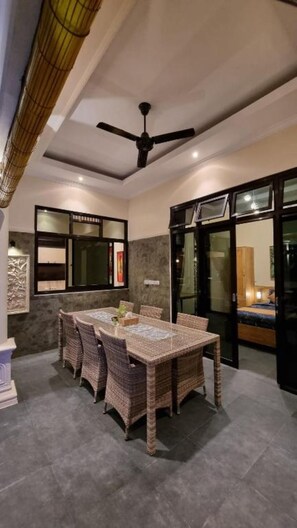 A dining area with a table and chairs, a ceiling fan, and a view through a glass door. - Villa Kupu-Kupu 2B – Charming Private Pool Villa in Lovina (Buleleng)