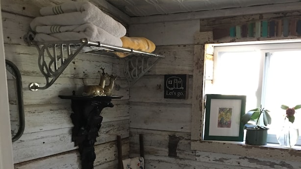 Casa de banho rústica com sanita branca, um armário com toalhas, um quadro emoldurado e uma janela com uma planta.