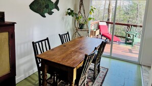 Uma área de refeições com mesa e cadeiras de madeira, uma obra de arte de parede com tema de peixe e vista para o exterior através de uma porta de vidro.