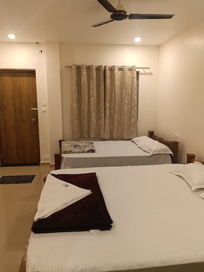 Habitación de hotel con dos camas, ventilador de techo y ventana con cortinas.